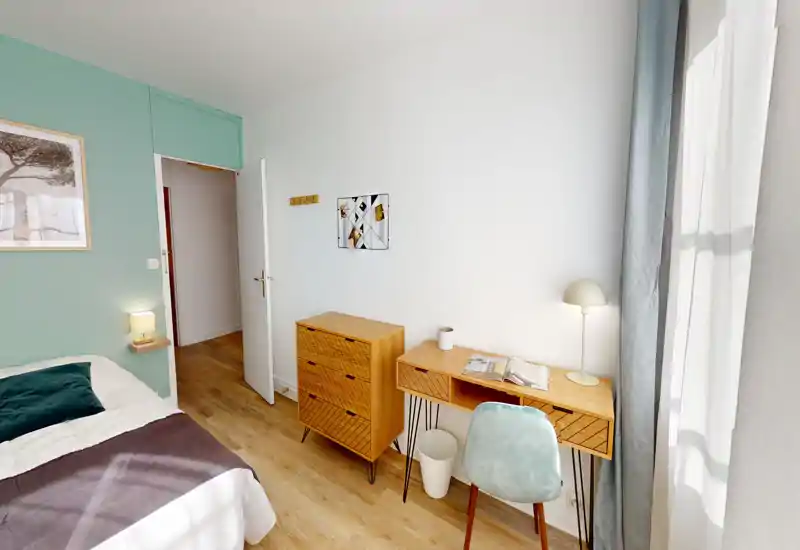 Bright, modern bedroom with a comfortable double bed partially visible, wooden desk and dresser by the window offering a cozy workspace and natural light.