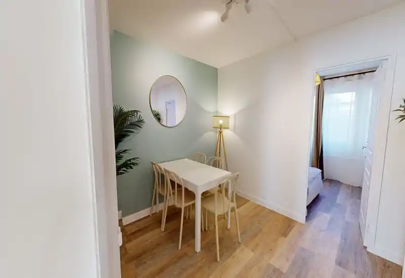 Small, stylish dining nook with a white table, four chairs, decorative round mirror and floor lamp creating a cozy, well-lit corner.