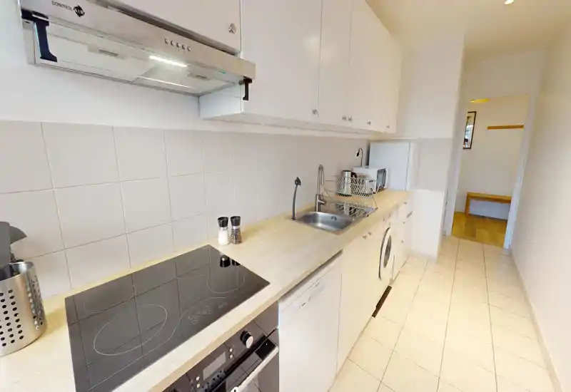 Bright galley kitchen with built-in hob, oven, sink and countertop appliances. Clean, functional layout ideal for small apartments.