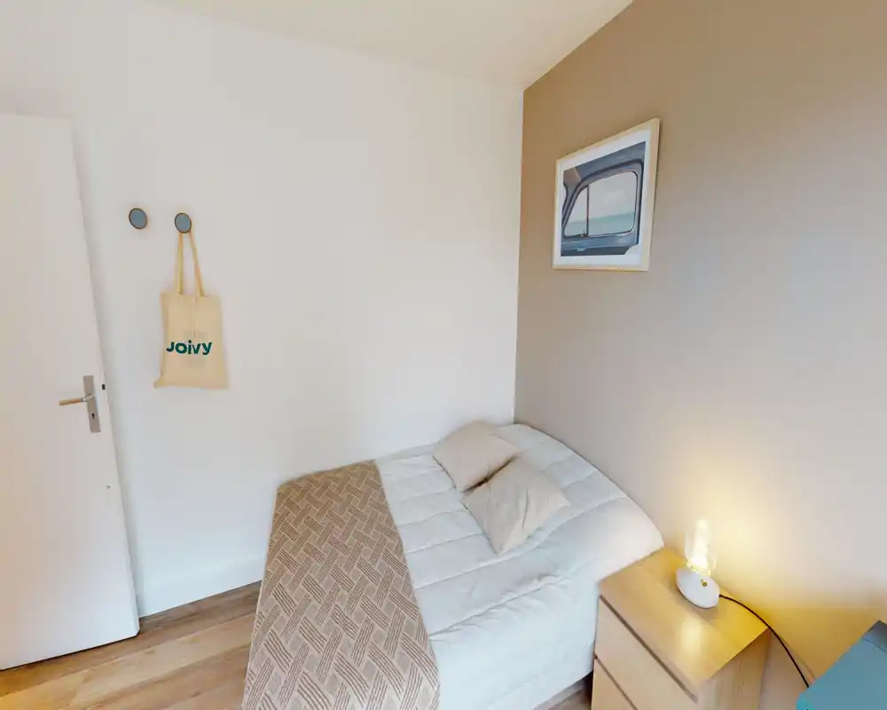 Chambre compacte et soignée avec lit double, literie douce, chevet avec lampe et décoration minimale et chaleureuse.