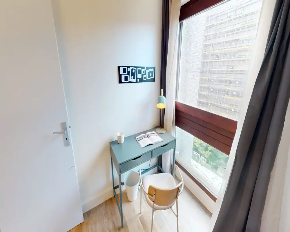 Coin bureau lumineux près de la fenêtre : un petit bureau avec lampe, chaise et un livre, idéal pour télétravail ou étude avec une belle lumière naturelle.