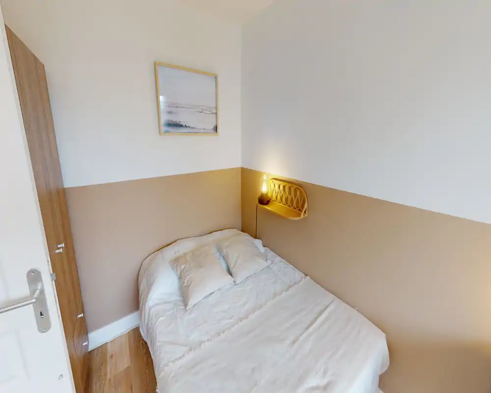 Petite chambre bien agencée avec un lit double, linge de lit doux et une lampe de chevet chaleureuse ; murs bicolores neutres pour une ambiance moderne et cosy.