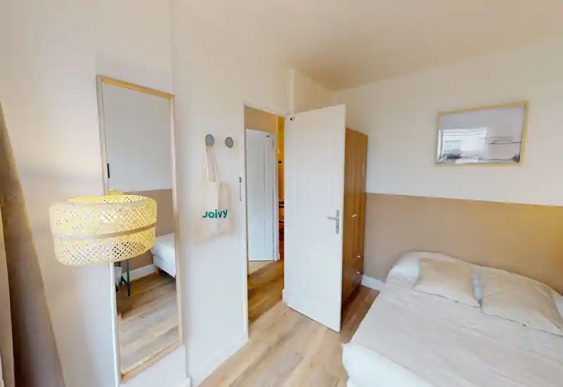 Bright, cozy small bedroom with a double bed, wooden flooring and neutral decor. A full-length mirror and soft lamp add depth and warmth to the space.