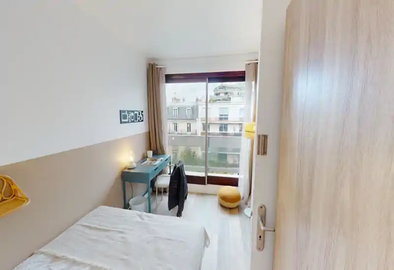 Bright, modern single bedroom with a comfortable bed, a desk by the window and large glass doors providing natural light and street views — ideal for a student or professional.