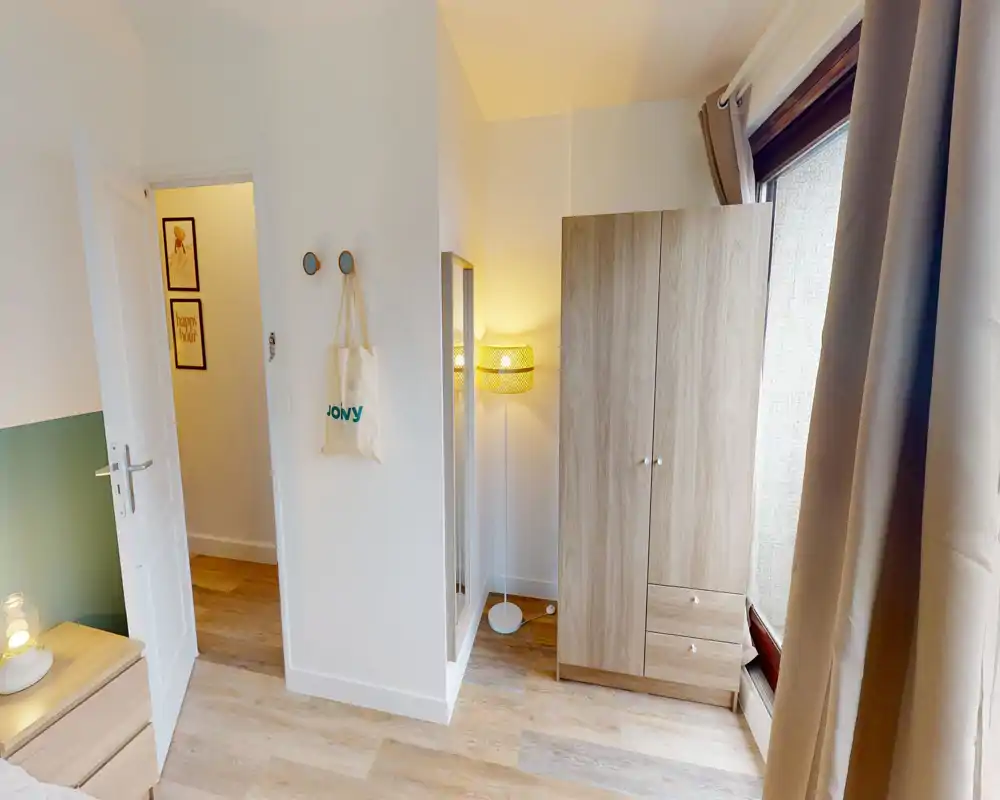 Coin de chambre bien éclairé avec armoire, table de chevet et vue partielle du lit ; une lampe chaude et des tons boisés neutres apportent une ambiance apaisante.