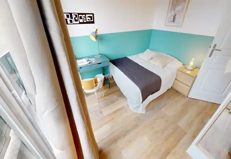 Bright, compact bedroom with a neatly made single bed, bedside table and a small desk by the window — ideal for a student or short-stay guest.