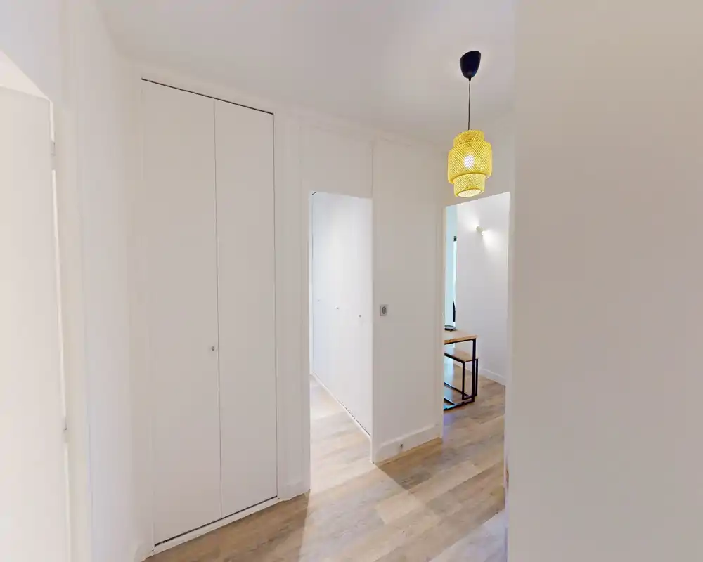 Entrée/couloir lumineux et moderne avec rangement intégré et sol effet bois ; murs blancs épurés et suspension décorative offrant une impression d'accueil.