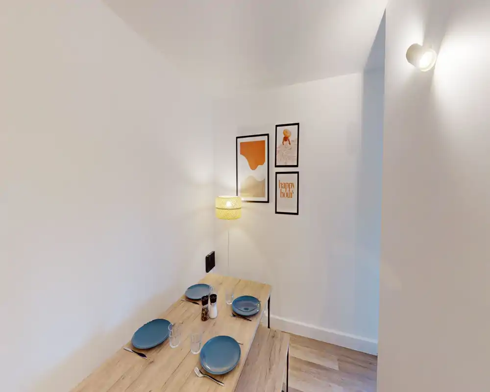 Coin repas chaleureux avec table en bois dressée pour quatre, cadres muraux et éclairage agréable — idéal pour repas décontractés.
