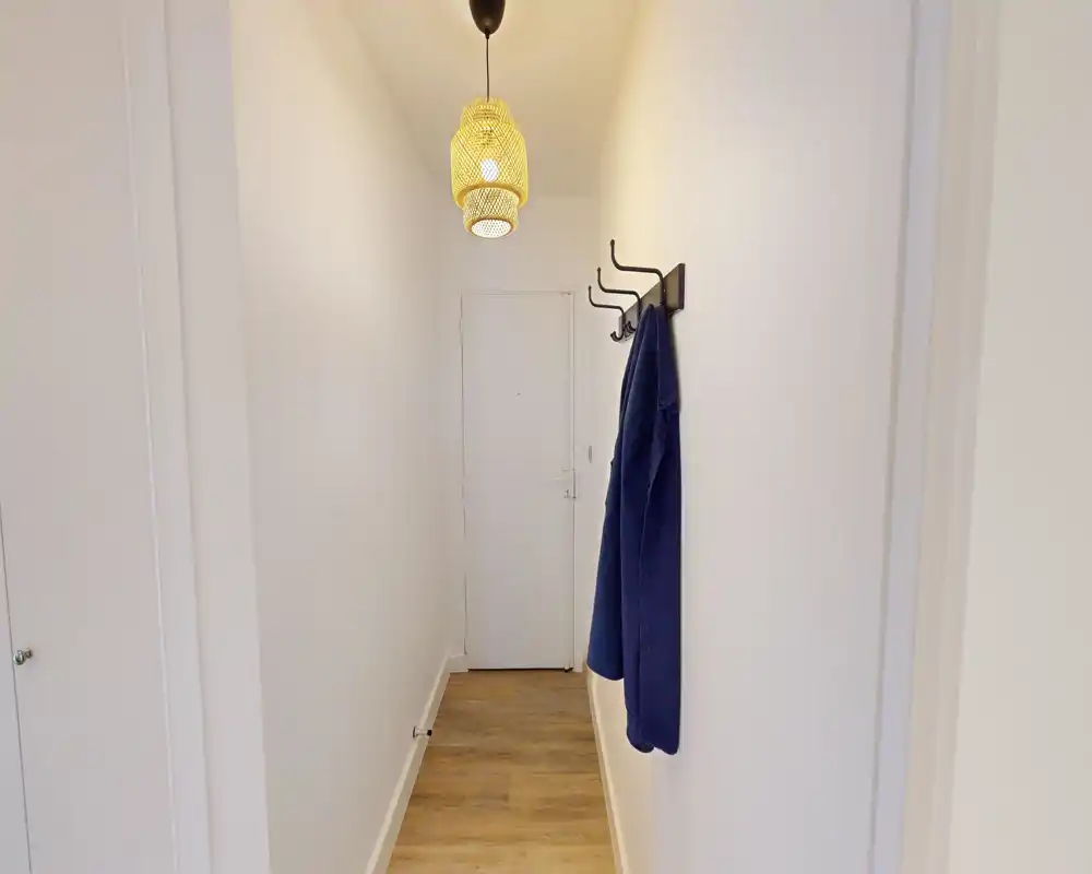 Entrée étroite et lumineuse avec sol en bois, patère murale et suspension décorative — couloir minimaliste adapté à un petit appartement.