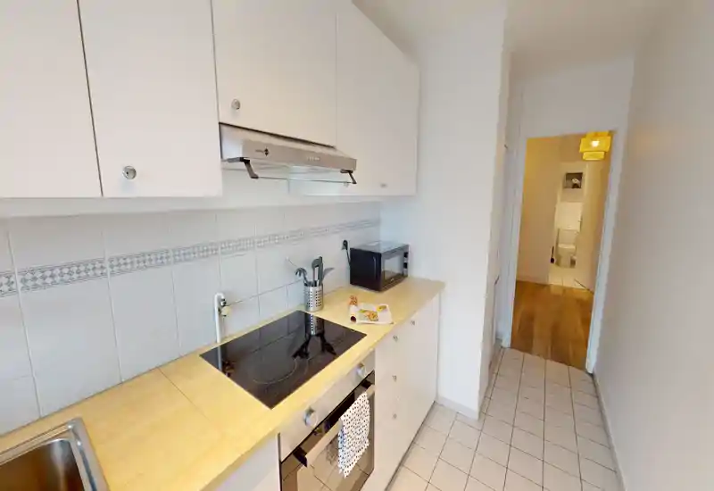 Compact modern kitchen with light wood countertops, white cabinets and an induction hob. Clean, well-lit galley layout ideal for short-stay rentals.