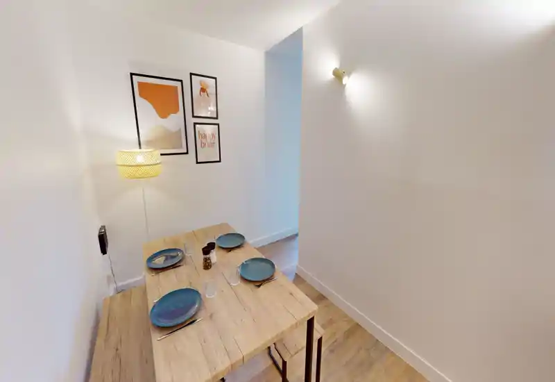 Compact dining area with a wooden table set for four, warm lamp lighting and modern wall art — ideal for cozy meals.
