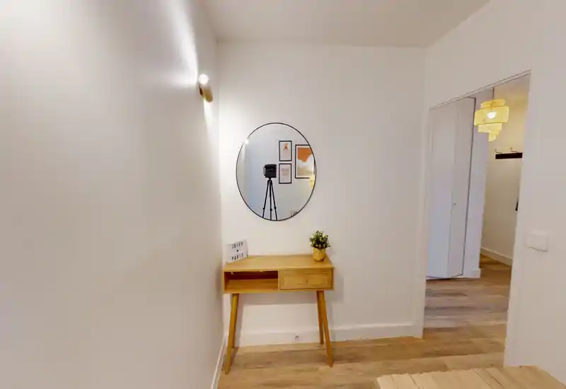 Minimal entrance hallway with a small wooden console table, round wall mirror and warm wooden flooring — clean, well-lit and welcoming.