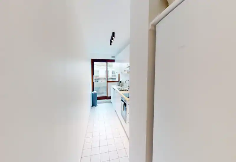 Bright narrow galley kitchen with white cabinets, tiled floor and a window/door providing natural light; compact layout ideal for efficient meal prep.