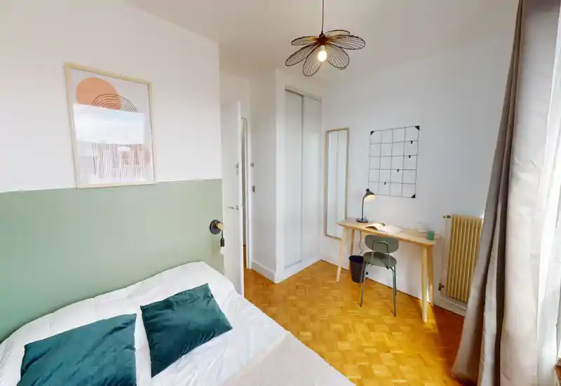 Bright, neatly styled bedroom with a double bed, green accent wall and a small desk by the window — ideal for both relaxing and working.