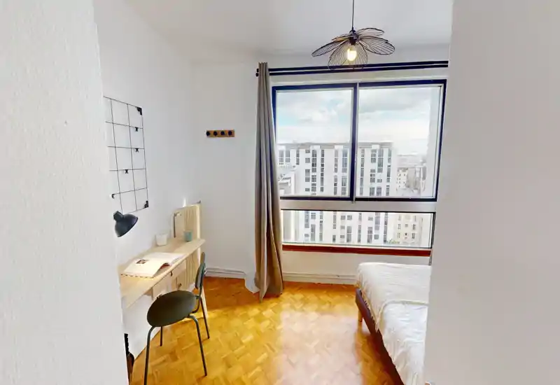 Bright, tidy bedroom with a large window providing city views, a small desk and chair, and a comfortable bed. Clean parquet flooring and minimal, modern decor make it ideal for a student or professional.