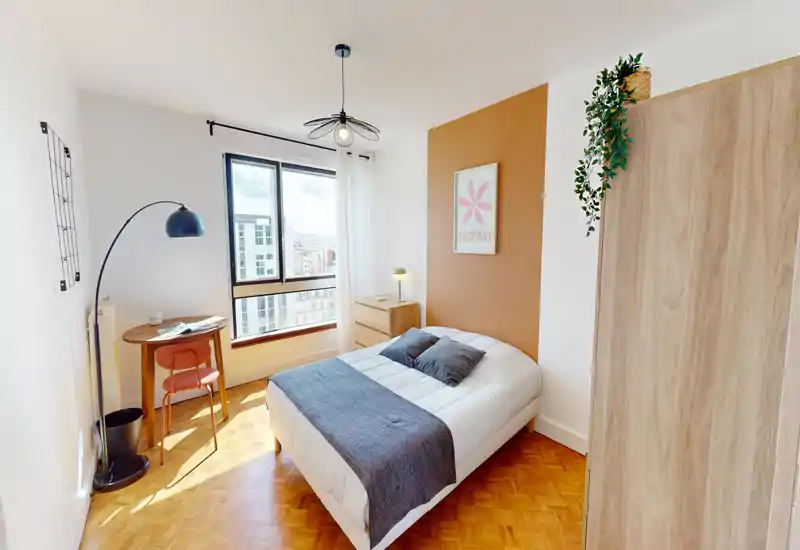 Camera da letto luminosa e ben arredata con un comodo letto matrimoniale, parete d'accento calda e angolo studio vicino alla finestra con molta luce naturale.