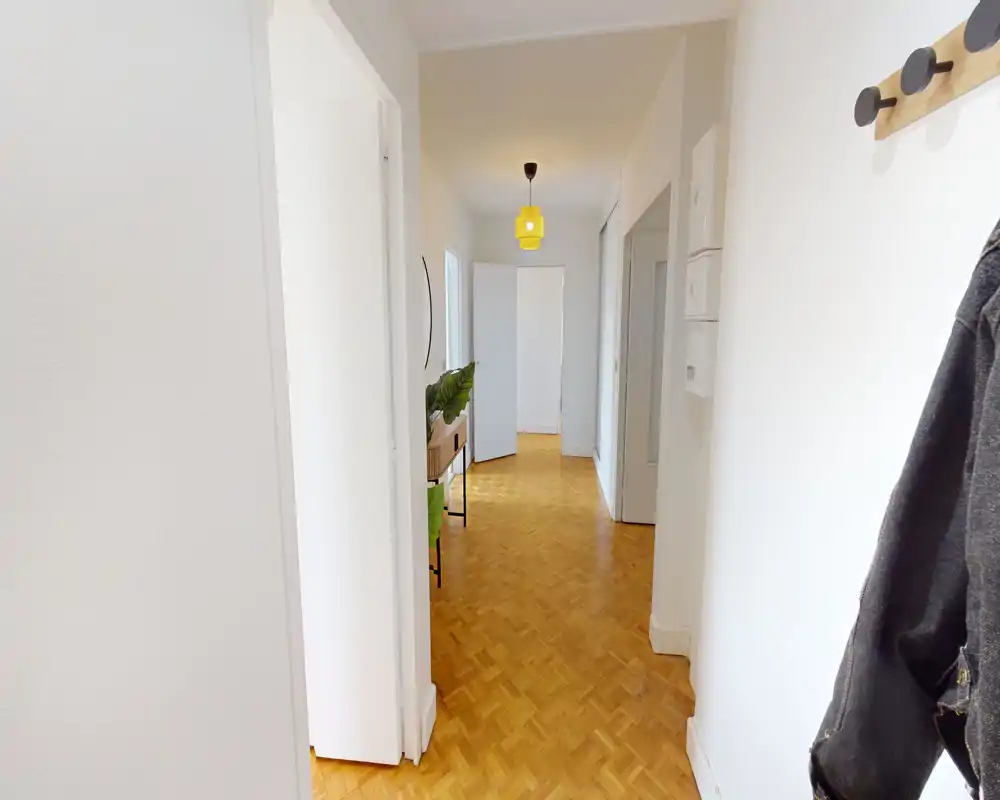 Bright, well-lit entrance hallway with parquet flooring, wall hooks and a small console table visible down the corridor — clean and welcoming entry space.