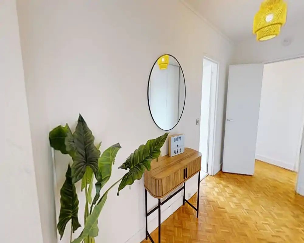 Bright, minimal entrance hallway with a small console table, round wall mirror and decorative plant; parquet flooring and white walls create a welcoming first impression.