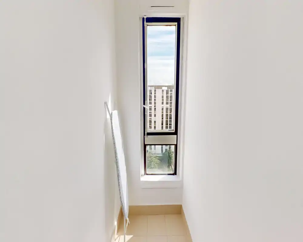 Narrow light-filled alcove with a tall window framing an exterior view — minimal balcony/terrace presence but plenty of natural light and a city outlook.