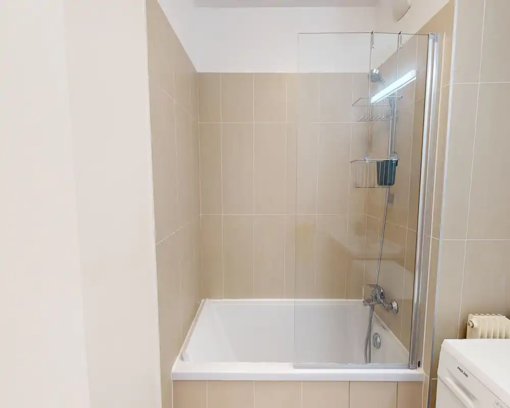 Modern tiled bathroom with a bathtub and glass shower screen, chrome fixtures and neutral beige tiles. Clean, bright and practical space ideal for rental listings.