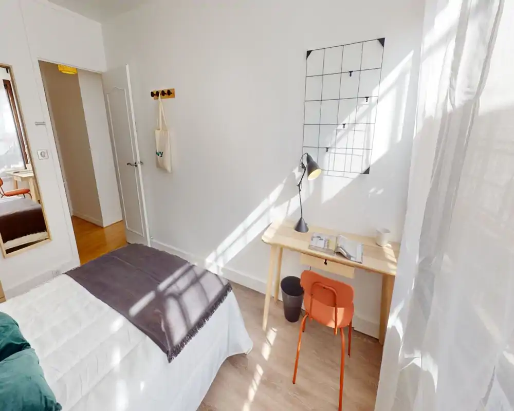 Bright, minimal bedroom with a comfortable double bed, a small wooden desk and a sunny window — ideal for a single occupant or a couple who like a clean, airy space.