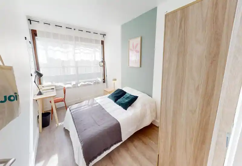 Bright, modern single bedroom with a neatly made bed, bedside table and desk by a large window letting in abundant natural light — ideal for a comfortable stay or student rental.
