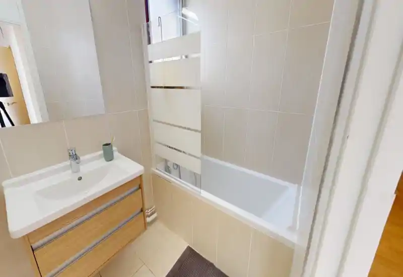 Salle de bain moderne et lumineuse avec baignoire et meuble vasque. Carrelage neutre et pare-douche en verre pour un rendu propre et contemporain.