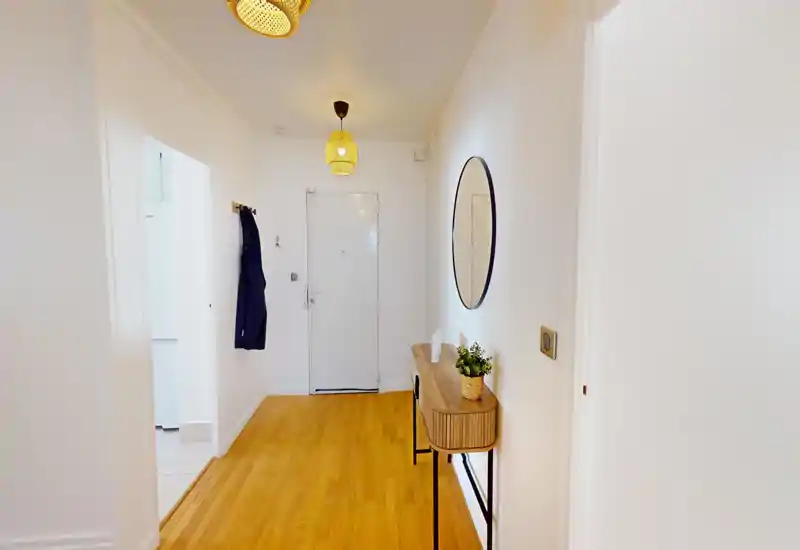 Entrée lumineuse et soignée avec sol en bois, patères murales, une console fine et un miroir rond — un espace d'accueil accueillant.