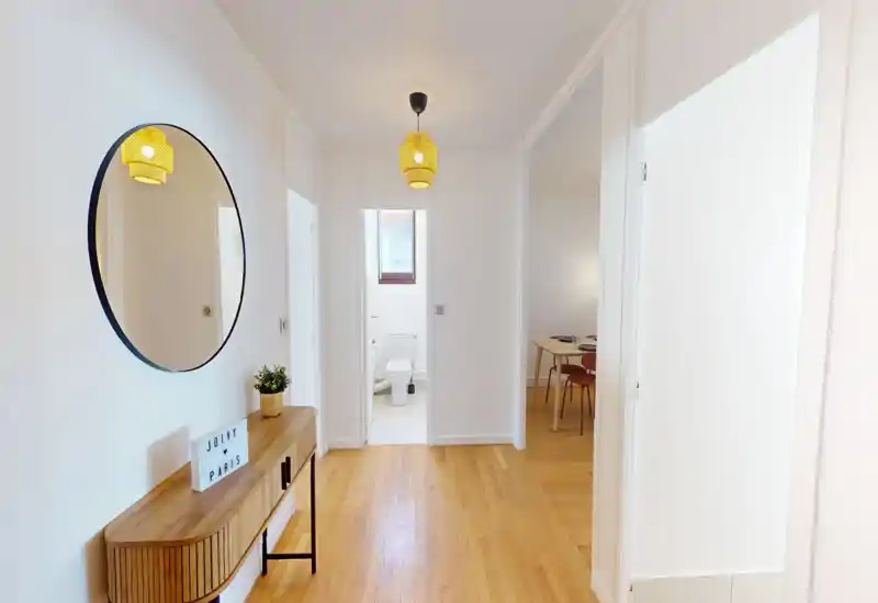 Entrée lumineuse et accueillante avec une console en bois, un grand miroir rond et un éclairage suspendu chaleureux ; vue dégagée sur les pièces adjacentes.