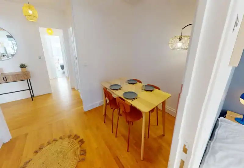 Well-lit dining area with a wooden table set for four, warm wood flooring and a decorative pendant lamp — ideal for meals and small gatherings.
