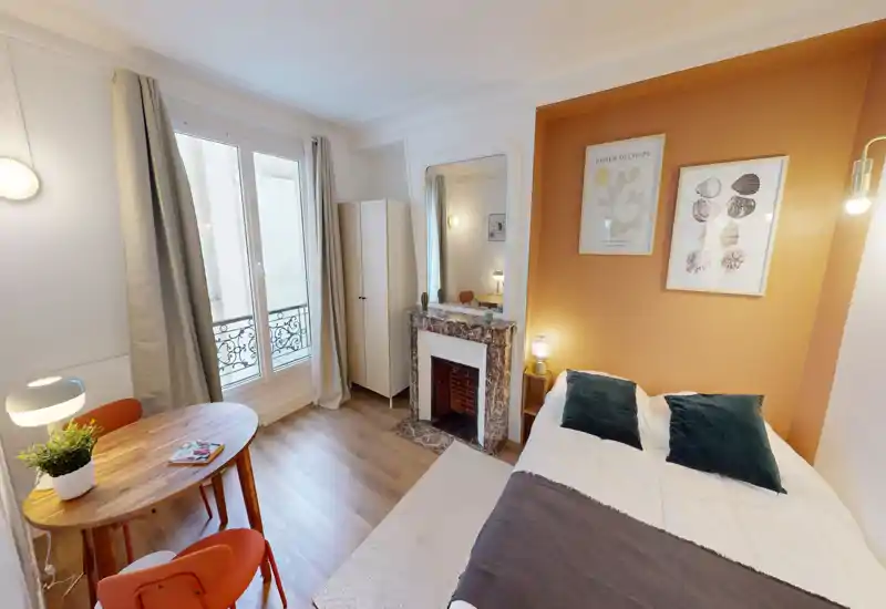 Chambre lumineuse et bien aménagée avec un lit double confortable, un mur d'accent chaleureux et une cheminée décorative. La lumière naturelle et les textiles donnent une atmosphère accueillante.