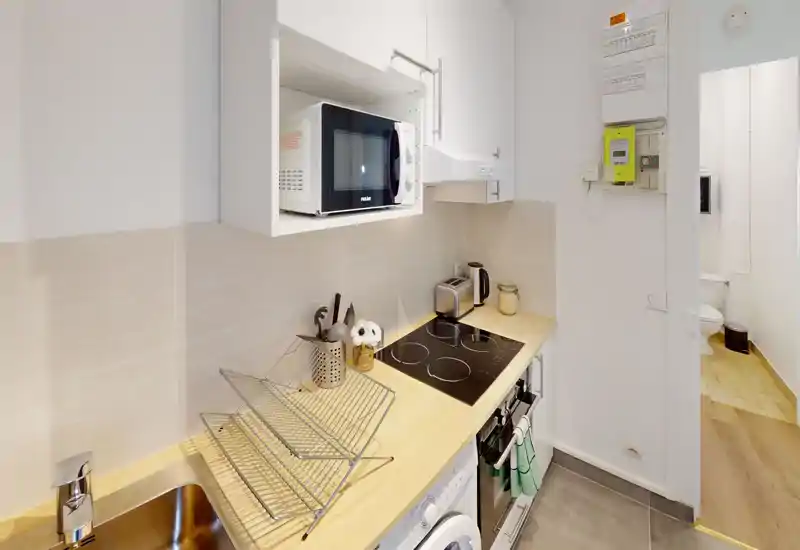 Cuisine moderne et compacte avec plan de travail en bois, plaque à induction, micro-ondes, évier et petits appareils ; lumineuse et bien rangée, adaptée aux locations courte durée.