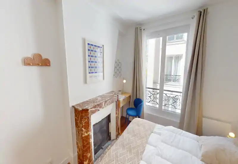 Chambre lumineuse et accueillante avec un lit confortable, une cheminée en marbre décorative et un petit bureau près de la fenêtre bénéficiant de la lumière naturelle.