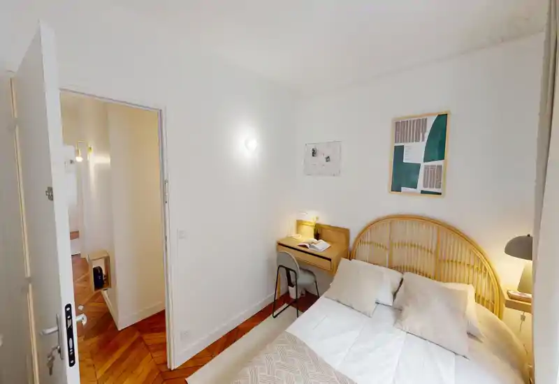 Chambre lumineuse et chaleureuse avec une tête de lit en rotin, lampes de chevet et petit bureau — linge propre et parquet chaleureux.