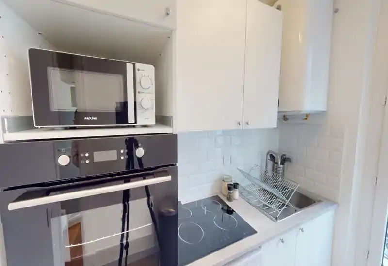 Cuisine compacte et moderne avec four encastré, micro-ondes et plaque à induction ; meubles blancs et crédence en carrelage métro pour un rendu lumineux et net.