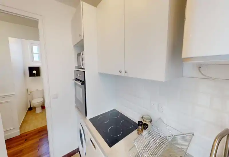 Cuisine compacte et lumineuse type couloir avec plaque à induction, four et micro-ondes encastrés, placards supérieurs et égouttoir en acier; dosseret en carreaux métro blancs et aménagement optimisé.