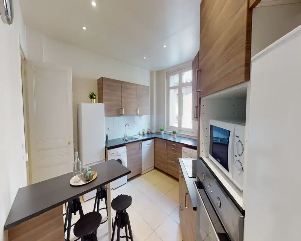 Cuisine moderne et lumineuse avec placards effet bois, appareils intégrés, un comptoir breakfast et une grande fenêtre apportant de la lumière naturelle.