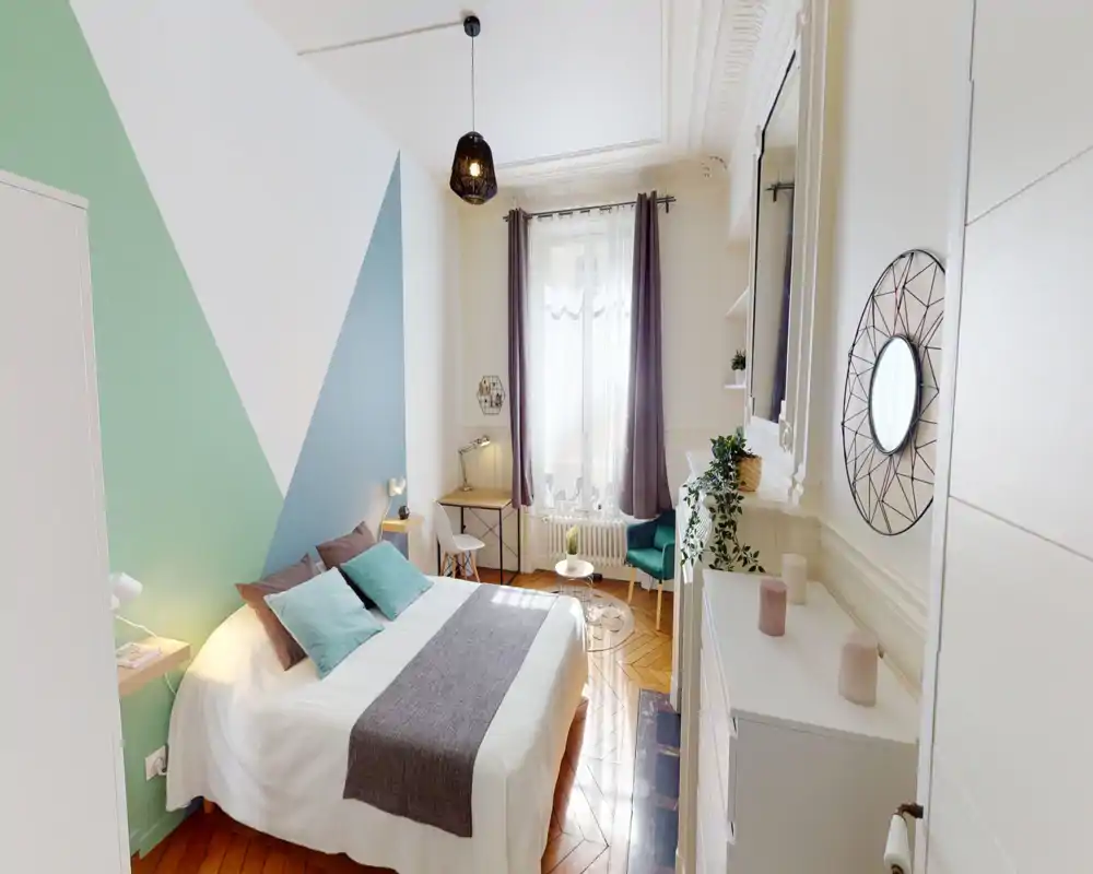 Camera da letto luminosa e di design con letto matrimoniale, parete geometrica dipinta, tessili morbidi, scrivania vicino alla finestra e piante decorative — uno spazio accogliente e ideale per rilassarsi o lavorare.