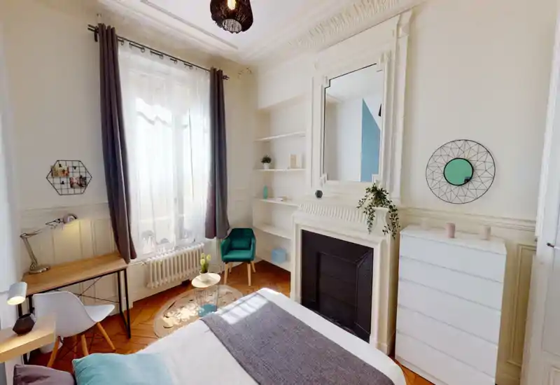 Camera da letto luminosa e di stile con ampia finestra, camino decorativo e letto ben rifatto. Tessuti morbidi, una poltrona accogliente e scaffali curati creano un’atmosfera invitante, perfetta per un annuncio.