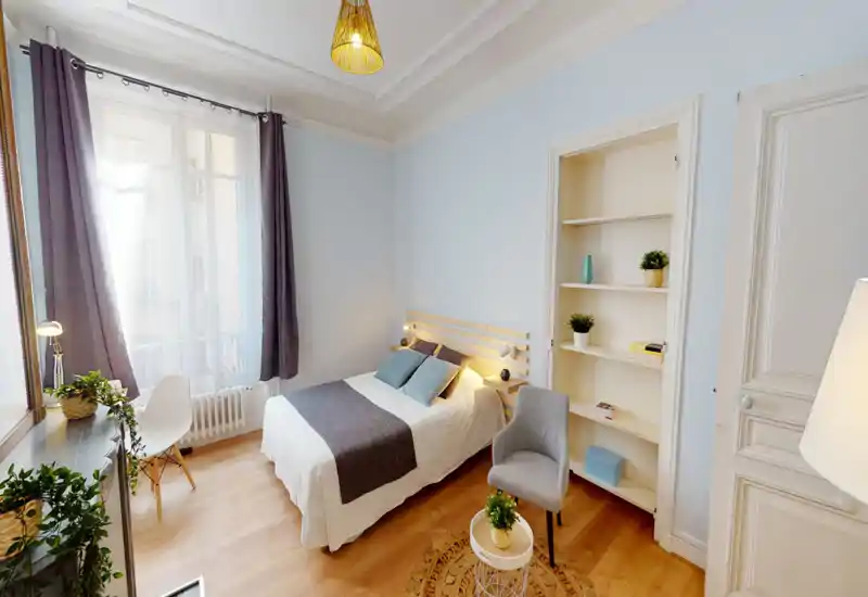 Camera da letto luminosa e ben arredata con letto matrimoniale, tessili morbidi e luce naturale da una grande finestra; scaffalatura semplice e una poltroncina accogliente.