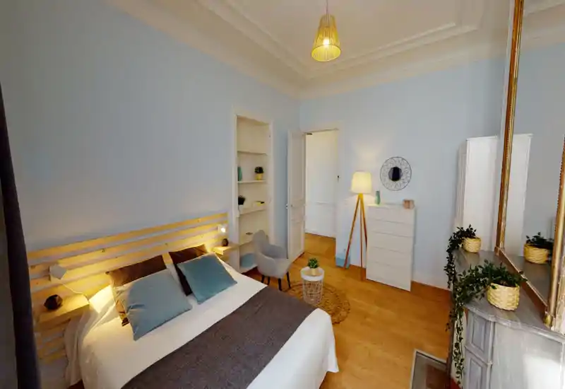 Camera da letto luminosa e ben arredata con ampio letto matrimoniale, cuscini morbidi, testiera in legno e luci calde che creano un’atmosfera accogliente.