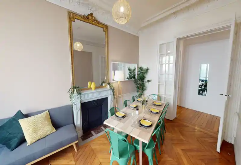 Zona giorno luminosa e di stile con grande specchio sopra il camino decorativo, divano accogliente e tavolo in legno apparecchiato — perfetta per pranzi conviviali e relax.