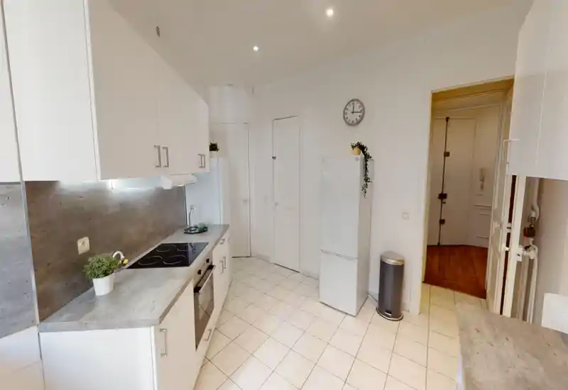 Cuisine moderne et lumineuse avec meubles blancs, four encastré et plaque vitrocéramique, sol carrelé clair et réfrigérateur indépendant — espace propre et fonctionnel avec de petites plantes pour une touche de fraîcheur.