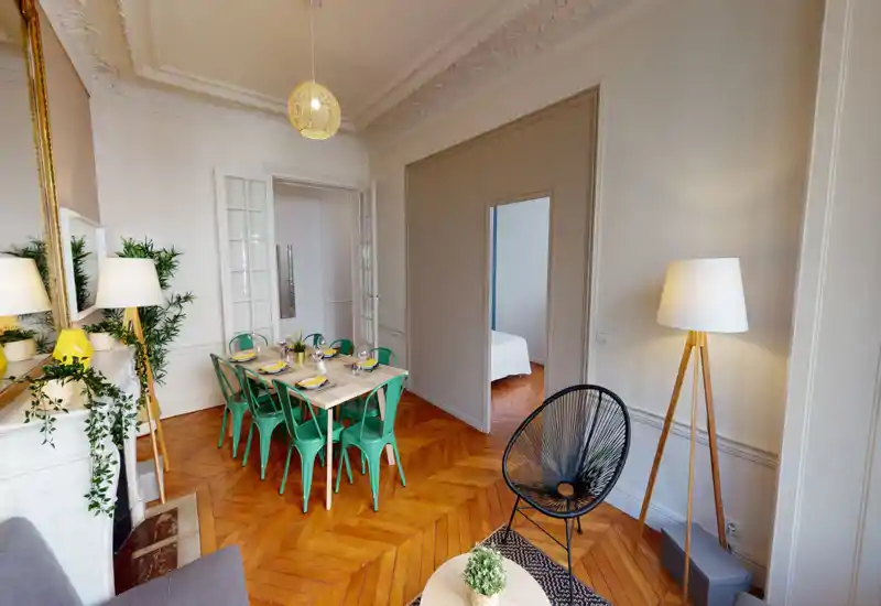 Grand espace salon/salle à manger élégant avec parquet en chevron, table dressée pour six avec chaises vertes, plantes décoratives et éclairage chaleureux — un espace ouvert accueillant.