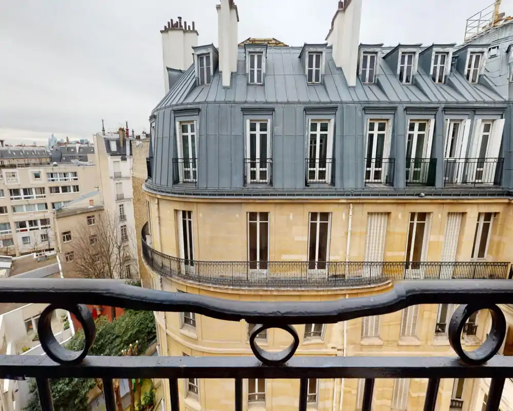 Balcon offrant une vue sur une façade parisienne typique avec garde-corps en fer forgé et toit mansardé — perspective extérieure lumineuse idéale pour mettre en valeur la vue.