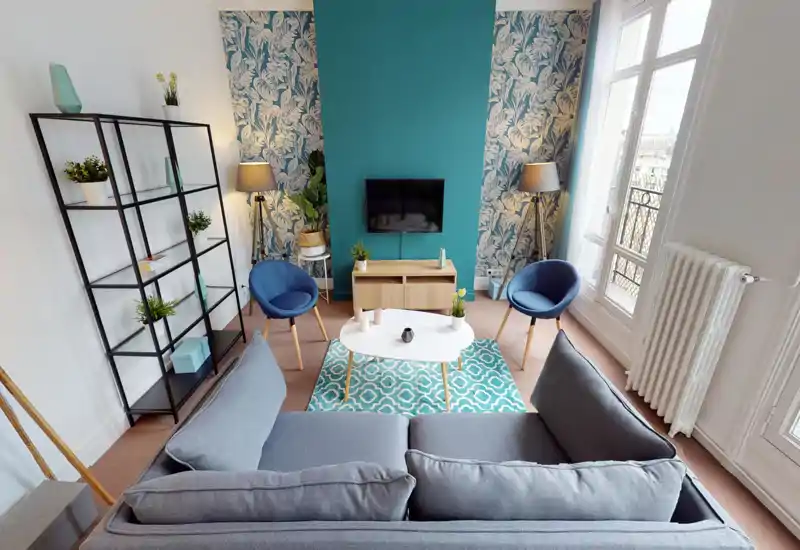 Salon lumineux et élégant avec grand canapé face à la TV murale, deux fauteuils bleus, étagère décorative et tapis à motifs — idéal pour se détendre ou recevoir.