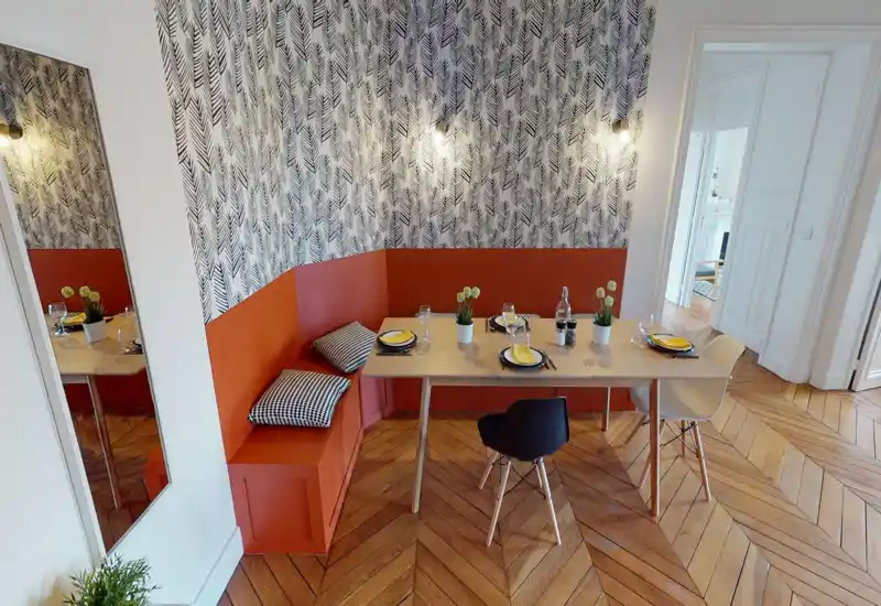 Coin repas élégant avec banquette intégrée orange, table en bois et chaises mixtes ; table dressée pour quatre avec plantes décoratives et parquet chaleureux.