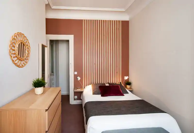 Bright, stylish bedroom with a full double bed, coordinated pillows and warm wooden accents. The vertical wood slats behind the bed and matching furniture create a cozy, modern feel ideal for rental listings.