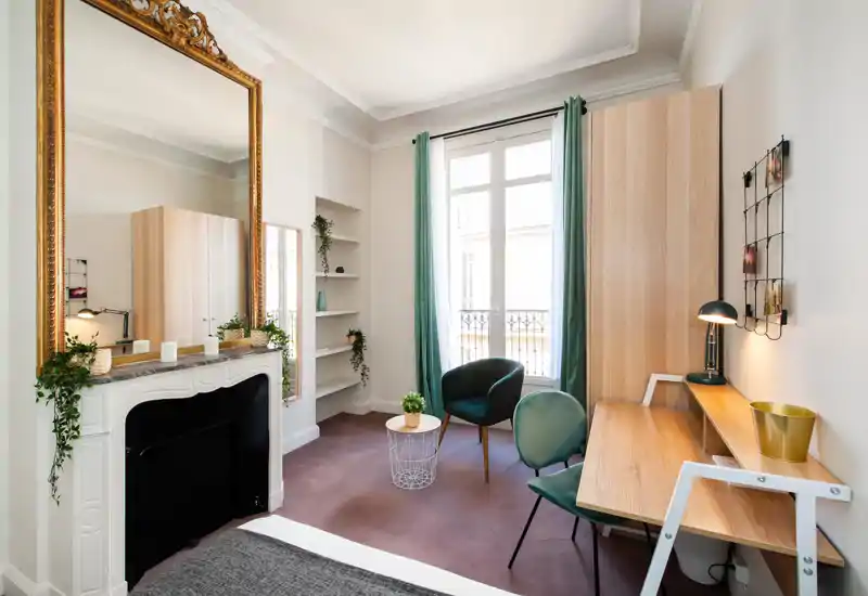 Chambre lumineuse et élégante avec lit visible, cheminée décorative et bureau près de la fenêtre — idéale pour travailler et se détendre.