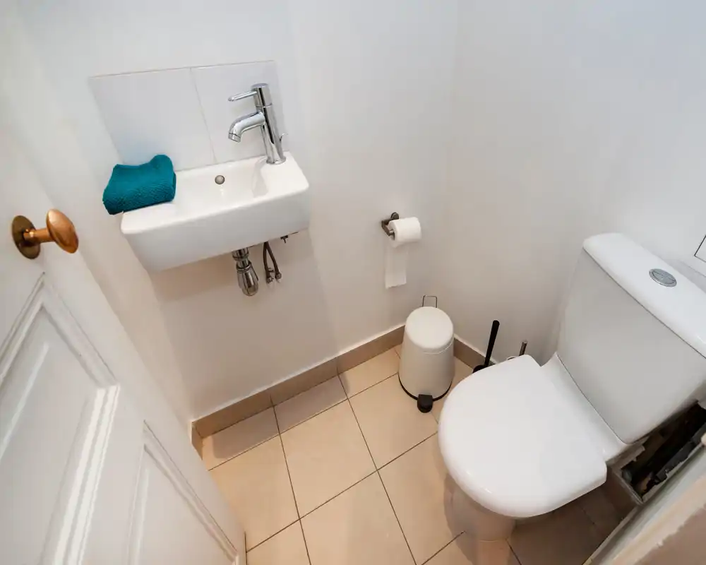 Petite salle de bain propre avec toilette, lavabo mural et carrelage au sol — lumineuse et au style minimaliste.